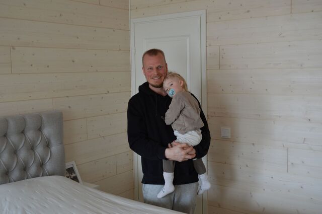 Mies pitää lasta sylissään makuuhuoneessa, joka on remontoitu Luova-sisustuspaneeleita käyttäen.